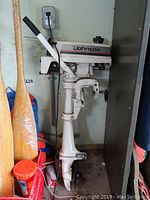 Johnson Colt outboard motor leaning against wall showing throttle handle, controls and propeller