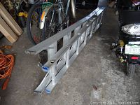Full view of the aluminum combination ladder folded and resting on the floor next to bicycles and a motorcycle.