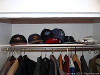 Row of ball caps of various colors and logos on a shelf above coat rack with jackets hanging below.