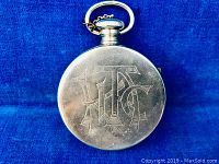 Front view of silver-tone pocket watch with engraved monogram on cover, showing design and condition of the front.