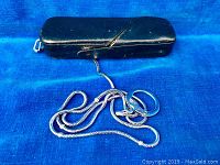 Black leather protective camera case with attached silver chain and keyring lying on blue fabric background.