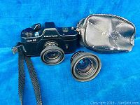 Pentax Auto 110 camera with lens attached, additional lens and carrying case on blue background