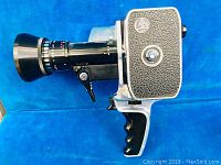 Side profile of vintage Bolex Paillard 8mm movie camera with lens and pistol grip handle on blue background