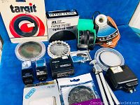 Wide shot showing all items and boxes included in the lot arranged on blue fabric background. Highlights included Targit lens hood box, Hakuba optical filter box, Zeiss Ikoblitz flashes, Argus Genesis II flash, assorted filters, and tripod.