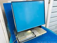Front angled view of the small desktop microfiche viewer showing the blue screen and base with control panel and viewing area.
