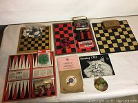 Photo of three game sets including chess and checkers boards, wooden chess pieces in bag, red and black checkers pieces in containers, backgammon set with dice, and additional game accessories