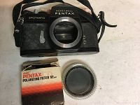 Honeywell Pentax Spotmatic camera body and new Asahi Pentax polarizing filter with box displayed on flat surface.