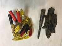 Photo of yellow auto jumper cables with red and black clamps alongside a black metal scissor jack, showing both items clearly on a light-colored surface.