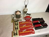Photo of hanging bird feeder, old decorative lamp glued back together, PT Plotts Bus Co. teapot (new), wall-mounted electric light, three Bausch & Lomb slide trays for slides, and three Warps storm window kits