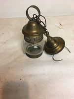 Older brass hanging lamp with glass globe and detached brass ceiling mount on white surface