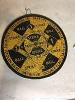 Photo of one side of the double-sided dart board featuring baseball score terms in yellow and black with a hanging wire attached.