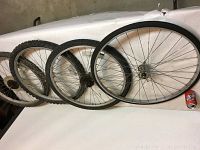 Four bicycle wheels and tires displayed side by side, showing tread and one new 27" tire.