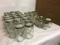 Photo showing 28 wide mouth clear glass Mason jars arranged on a table, including 20 quart-size jars and 8 pint-size jars.