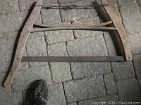 Old wood saw with two wooden handles and a metal blade lying on a stone floor.
