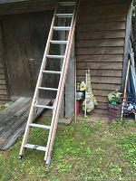 Side view of a 20 ft fiberglass ladder with aluminum steps leaning against a wooden wall near a shed, showing ladder feet and surroundings.