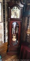Front view of grandfather clock showing ornate brass dial, clock case and glass door.