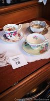 View of three bone china tea cups and saucers on wooden surface showing floral and ornate hand-painted designs, illustrating excellent condition.