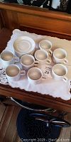 Set of 8 stacked white espresso cups with matching saucers arranged on a white cloth.