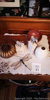 Photo of all collectible items arranged on a cloth: dragonfly hanger, two zebra tinker boxes, grease holder, red wooden dish, white vase, wicker holder, round patterned basket