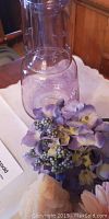 Close-up of light purple glass vase with artificial purple flower petals and berries.