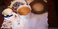 Top view of the decorative plate, ceramic planter, two-faced mug, and metal framed circular object on a white cloth