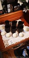 Set of six black ceramic coffee mugs and four white ceramic ramekins arranged on a cloth on wooden surface.