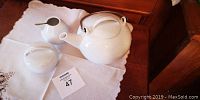 Photo showing entire tea set on white cloth including teapot, sugar bowl, and creamer.