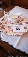 Photo showing the bone china creamer resting on the matching Royal Winston floral plate on a white fabric background.