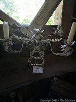Wide view of the 3-arm metal candle holder placed on a wooden surface, showing full design and wear.