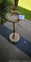 Full view of the antique metal ashtray stand with worn paint and round ashtray bowl on pedestal base.