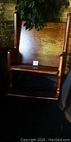 Overall frontal view of wooden church pew against brick wall with plant above backrest.