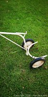 Side view of white metal lifting cart showing one wheel and part of curved base on grass