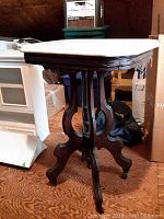 Full side view of antique side table showing marble top and dark wooden legs with visible scratches.
