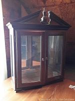 Front angled view of the wooden hanging cabinet showing glass doors and wood finish.