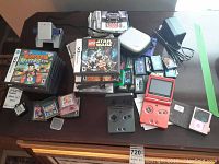 Overview of lot on table showing two SP consoles, game piles, charger, iPod and case