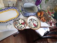 Serving dishes including trivet, platter, decorative basket with faux fruit, and tea set items on table