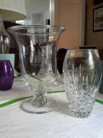 Wide flared Wedgwood crystal vase and shorter hand blown crystal vase together on white surface.