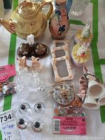 Photo showing the full assortment of decorative ceramics, salt and pepper shakers, photo frames, and confetti packets arranged on a table with a green-bordered cloth.