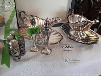 View of two silver-plate Gorham gravy boats each with scalloped underplates, two tall silver-plate salt and pepper shakers with pointed tops, four smaller silver-plate salt and pepper shakers with blue glass interiors.
