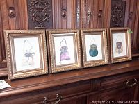 Four framed original canvas paintings by Peggy Abrams shown side-by-side with decorative gold frames on wooden surface.