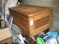 Two heavy wooden storage boxes with flat lids and child-safety hinges. Boxes show some exterior wear and natural wood grain. Positioned in a garage among household items.
