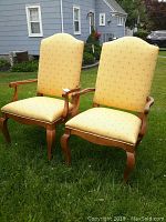 Two yellow upholstered high back wooden chairs positioned outdoors with slight wear on legs.