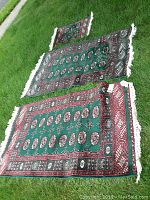 Photo showing two larger matching rugs laying on grass and a smaller rug above them, showcasing overall size and pattern.
