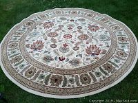 Photo showing full circular rug on grass background, revealing entire detailed floral pattern and border.