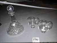 Wide angle view showing the decanter and two small pitchers on the ground with a MaxSold lot tag.