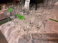 Two Oneida champagne flutes and twelve crystal wine glasses arranged on a table with visible height labels and tags