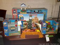 Photo showing complete Boulder Mountain Set with mountain structure, railway tracks, orange bridge-like structure, and two boxed accessories (Tidmouth Timber Yard and Rolf's Castle Bridge) on a wooden platform.