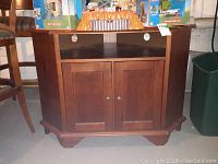 Front view of the wooden corner cabinet, showing two front doors with metal knobs, open top shelf, and some visible scratches on doors.