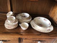 Photo showing entire 22-piece set including cups, plates, saucers, and serving bowl with floral pattern and gold trim, displayed on wooden surface