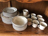 Full set of 8 cups, 8 saucers, 8 bowls with 8 dinner plates and 7 salad plates arranged on wood surface